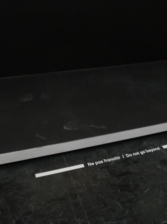 Une ligne blanche sur fond noir dans une expo pour signifier de ne pas dépasser la limite, avec des traces de pas de l'autre côté de ladite limite.